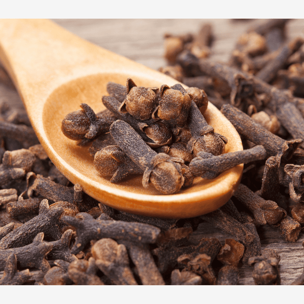 Cloves on a wooden spoon surrounded by cloves on a wooden surface. A helpful herb for wellness