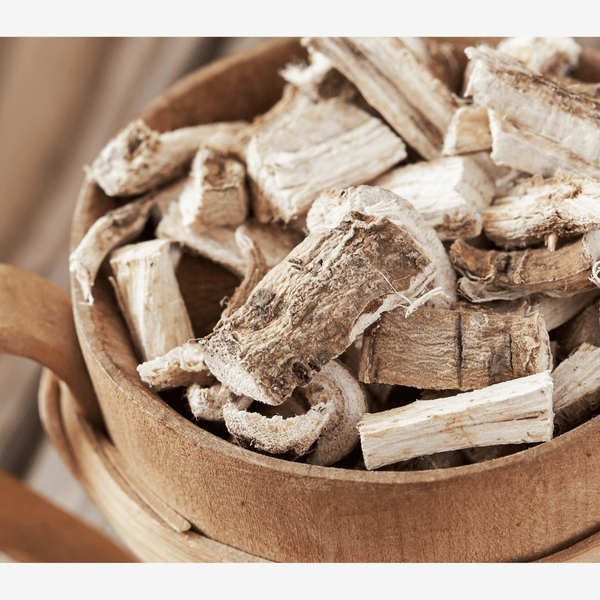 Wooden bowl filled with dried roots or herbs on a neutral background. A helpful herb for wellness